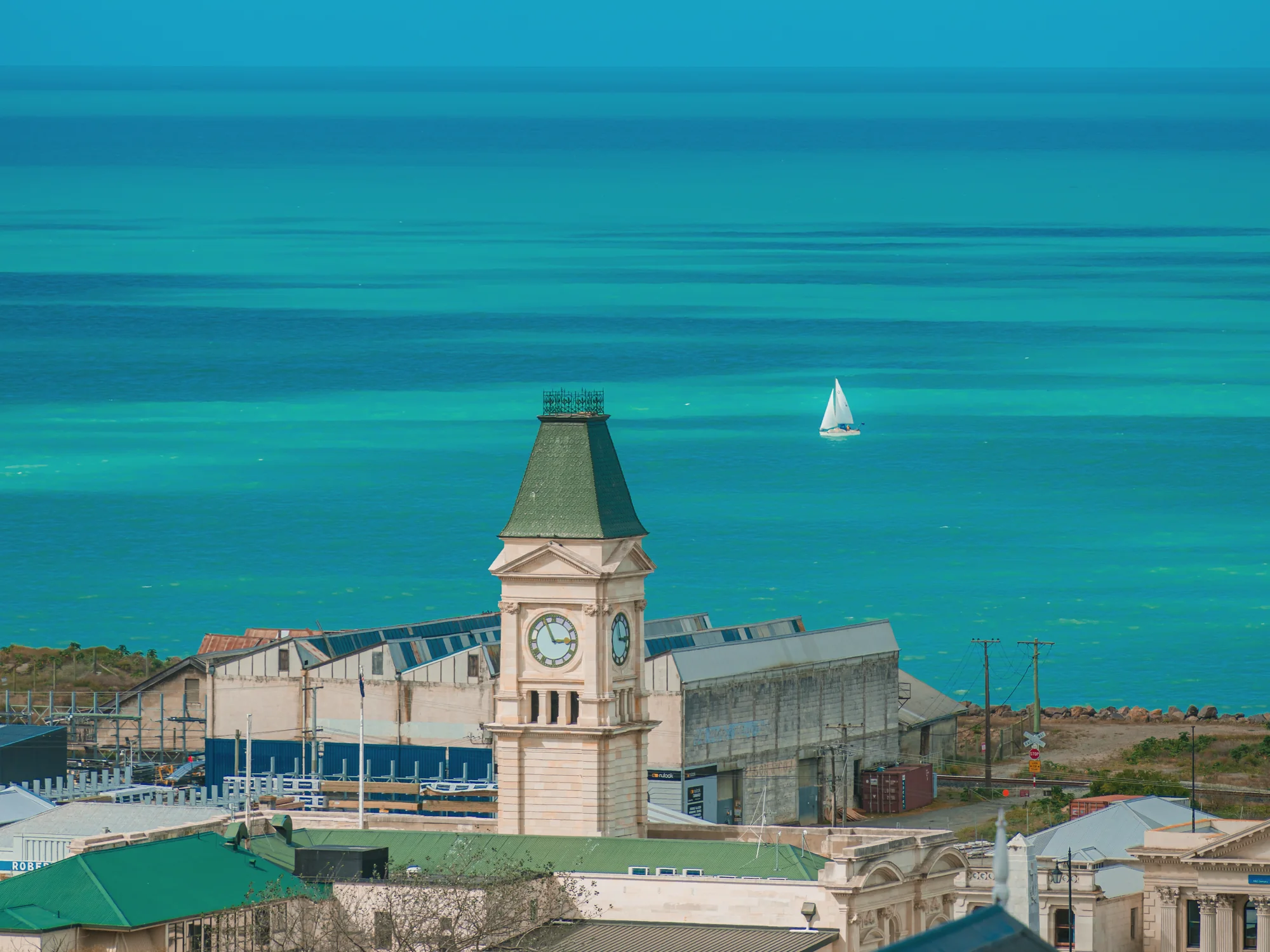 Oamaru’s harbour clock tower with a sailboat on the Pacific.