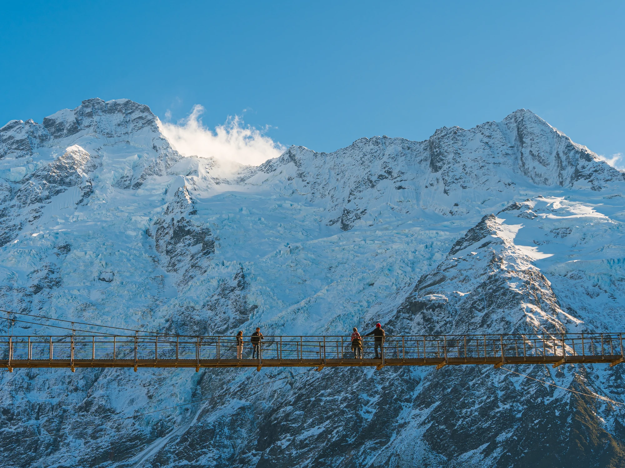 Hikers crossing a Hooker Valley suspension bridge